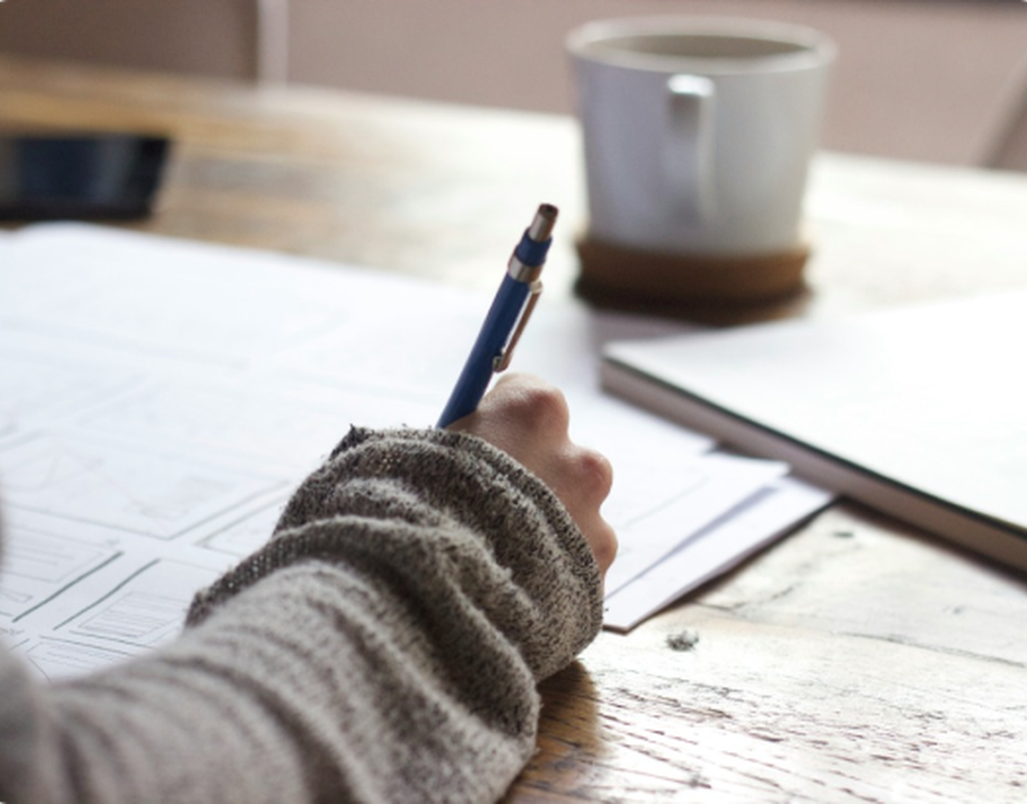 Hand writing notes with coffee cup in the background